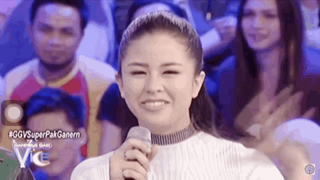 a woman is holding a microphone and smiling in front of a crowd .