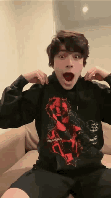 a young man is sitting on a couch wearing a black hoodie with a picture of a skull on it