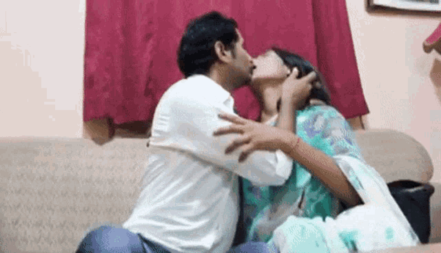 a man and woman are kissing on a couch in a living room .
