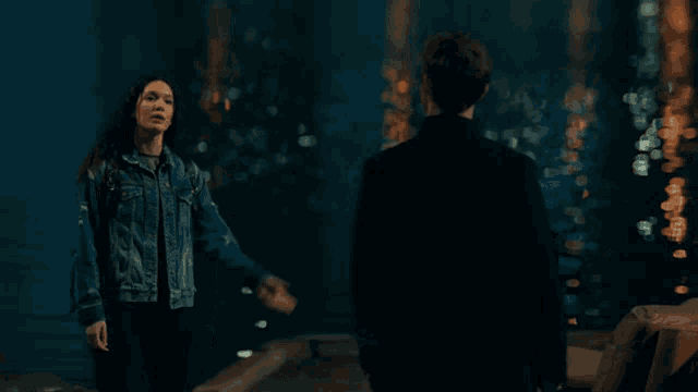 a woman in a denim jacket is standing next to a man in a black suit