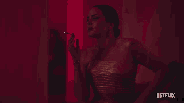 a woman in a strapless gold dress is standing in front of a red wall with netflix written on the bottom