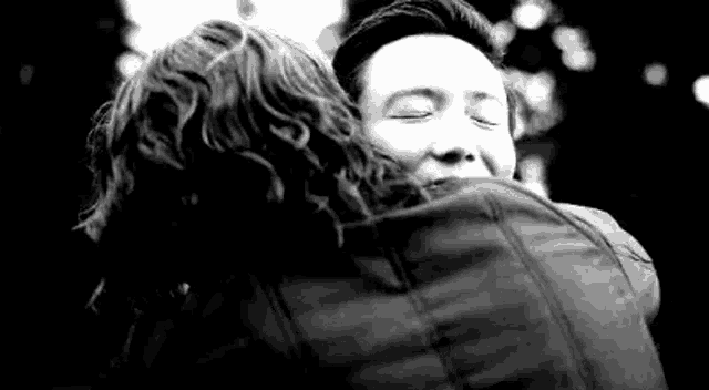 a black and white photo of a man and a woman hugging each other .