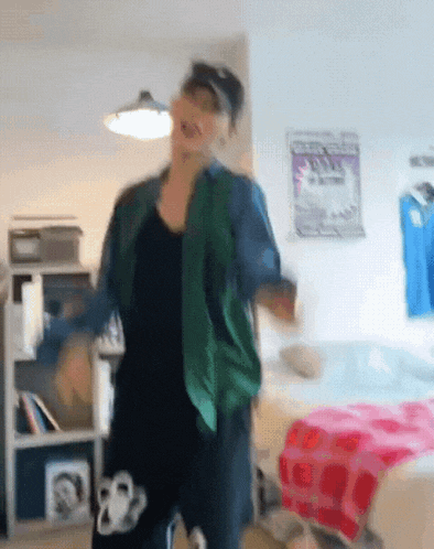 a woman in a green jacket is dancing in a room with a poster on the wall that says ' i love you '