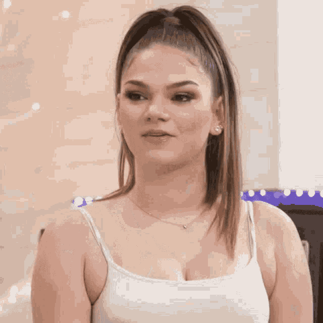 a woman wearing a white tank top and a necklace is smiling .