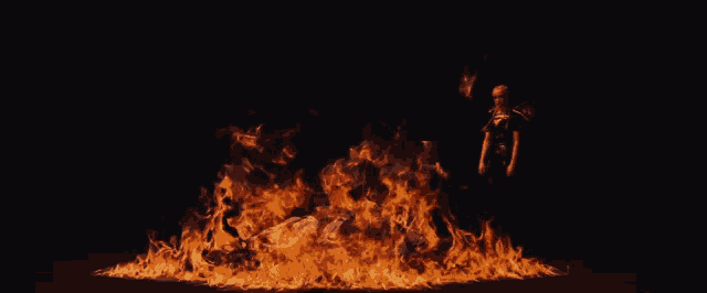 a woman stands in front of a large fire