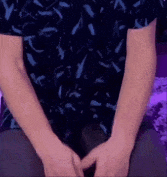 a man in a blue shirt is sitting on a couch with his hands folded .