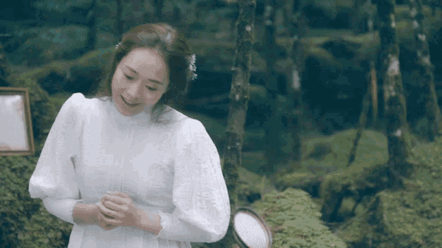 a woman in a white dress stands in the woods