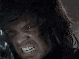 a close up of a man 's face with a beard and long hair making a funny face .