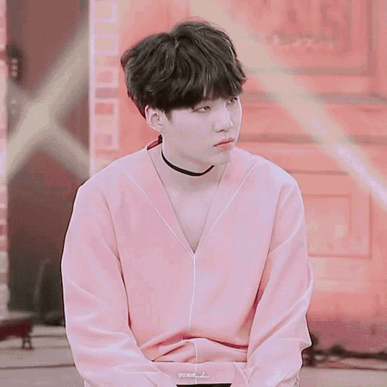 a young man wearing a choker and a pink shirt is sitting down .