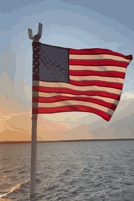 an american flag flies over a body of water at sunset