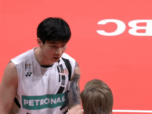 a man wearing a petronas jersey is talking to another man