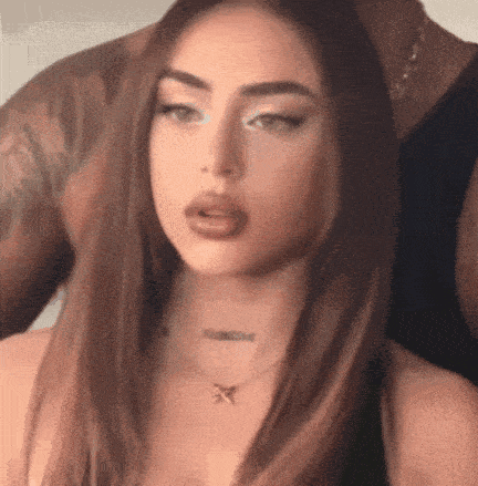 a woman with long brown hair and a necklace is sitting next to a man with tattoos on his arm .