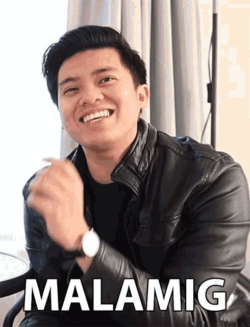 a man wearing a black leather jacket and a watch is smiling and the word malamig is on the bottom right