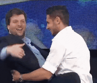 a man in a suit and tie is laughing with another man in a white shirt .