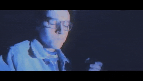 a man with glasses is smoking a cigarette in the dark .