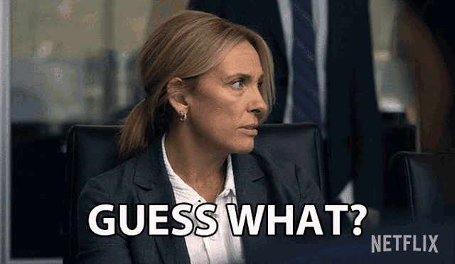 a woman in a suit and tie is sitting at a desk and says guess what