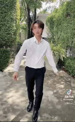 a man in a white shirt and black pants is walking down a sidewalk .