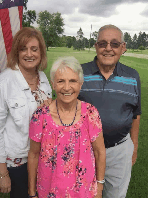 a man and two women pose for a picture with an american flag in the background