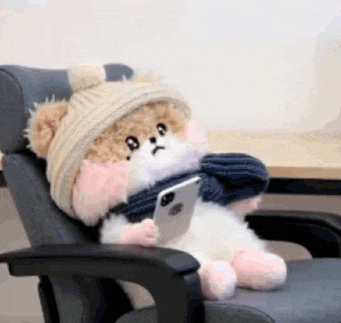 a stuffed animal wearing a hat and scarf is sitting in an office chair holding a cell phone .