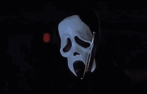 a man in a white shirt is sitting in front of a ghost mask .