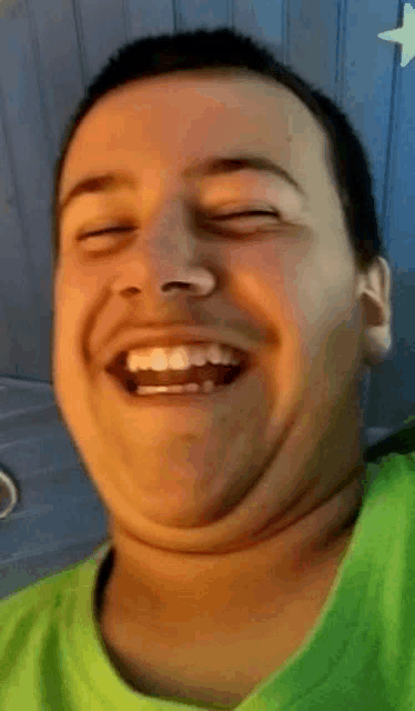 a man in a green shirt laughs with his eyes closed