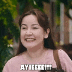 a woman in a pink shirt is smiling and saying ayieeee .