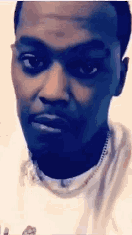 a man wearing a necklace and a white shirt is looking at the camera .