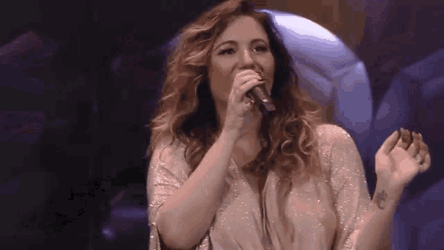 a woman is singing into a microphone on a stage with her hands in the air .