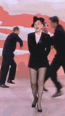 a woman in a black suit and hat is dancing on a stage .