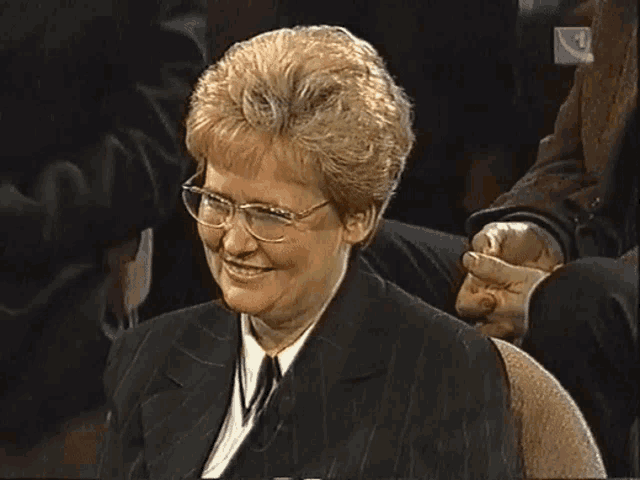 a woman wearing glasses and a suit is smiling in front of a sign that says k4
