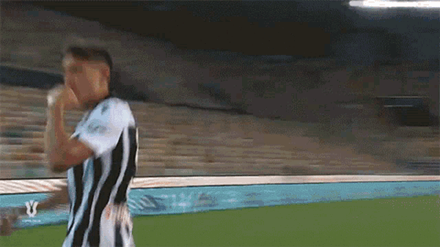 a man in a black and white striped shirt is walking on a soccer field .