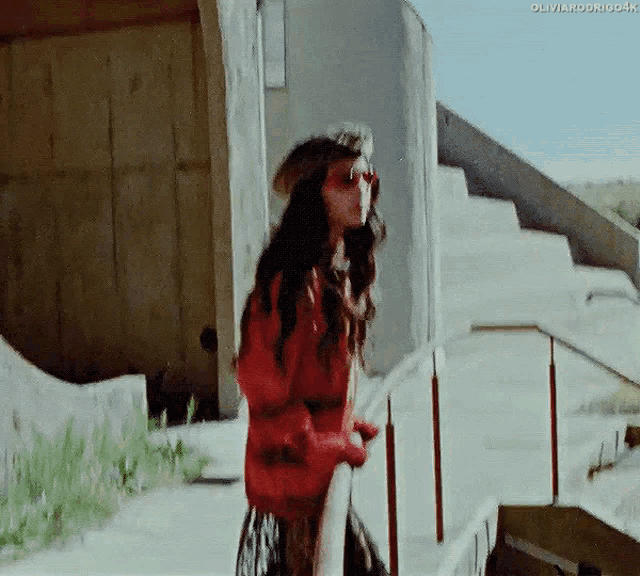a woman wearing a red jacket and sunglasses is standing on a railing .