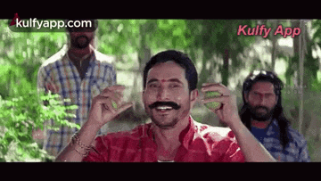 a man with a mustache is holding a lime in his hand while standing in front of a group of men .