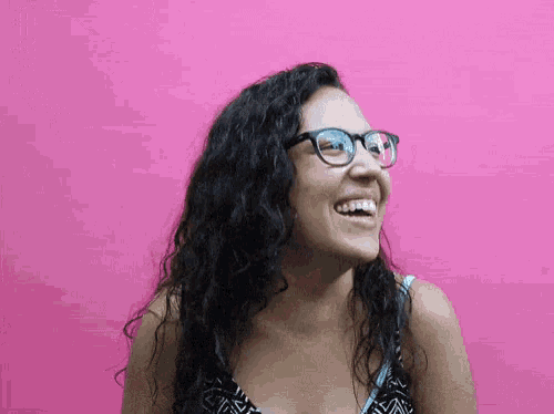 a woman wearing glasses is laughing in front of a pink wall