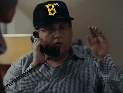 a man wearing a hat with the letter b on it talks on a phone