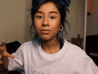 a woman with blue hair is wearing a white t-shirt and earrings