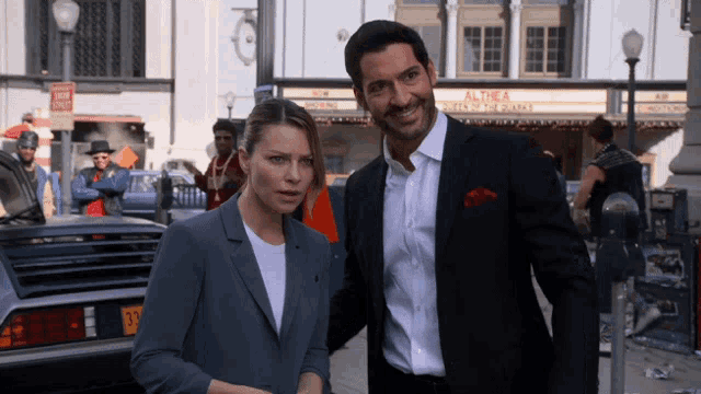 a man and a woman are standing in front of a building that has the word alpha on it