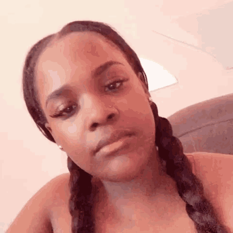 a woman with braids is sitting on a couch looking at the camera .