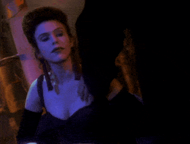 a woman wearing a black dress and black gloves is standing in a dark room