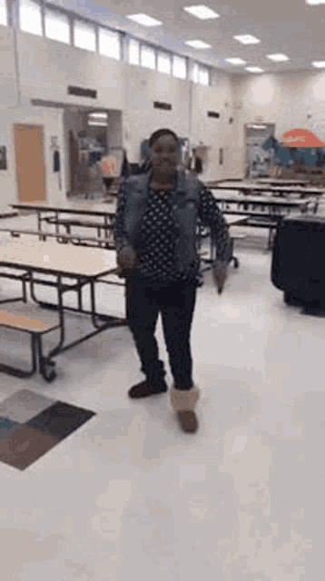 a woman is standing in a large room with tables and benches in a school cafeteria .