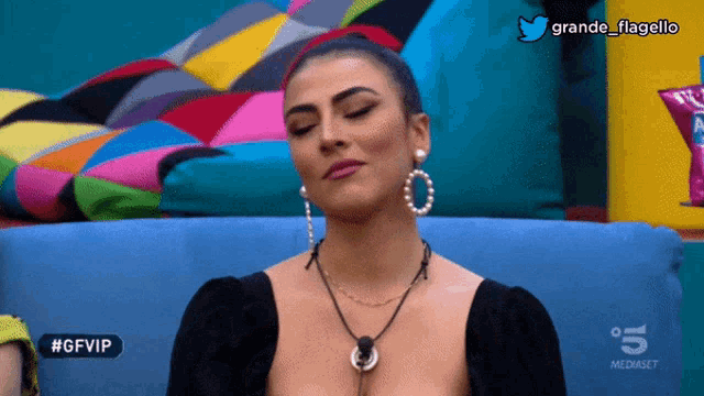 a woman sitting on a blue couch with #gfvip written on the screen