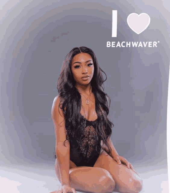 a woman in a black bodysuit is kneeling in front of a sign that says " i love beachwaver "
