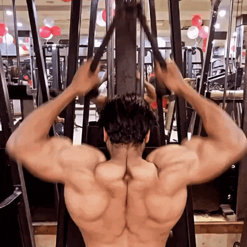 a muscular man is using a machine in a gym with balloons in the background