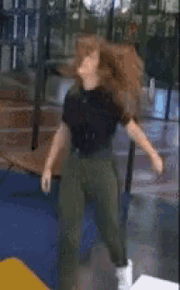 a woman in a black shirt and green pants is dancing in a room .