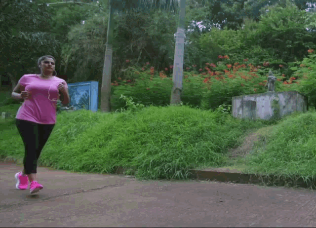 a woman in a pink t-shirt is jogging in a park