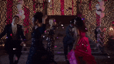 a group of people are dancing in front of a christmas tree while confetti is falling around them .