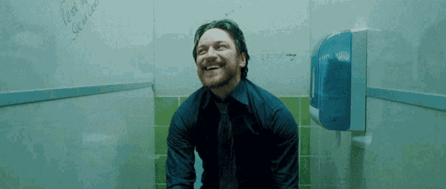 a man in a blue shirt and tie is sitting on a toilet with graffiti on the wall