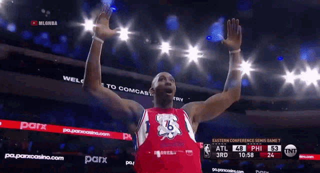 a basketball player wearing a 76 jersey stands in front of a scoreboard