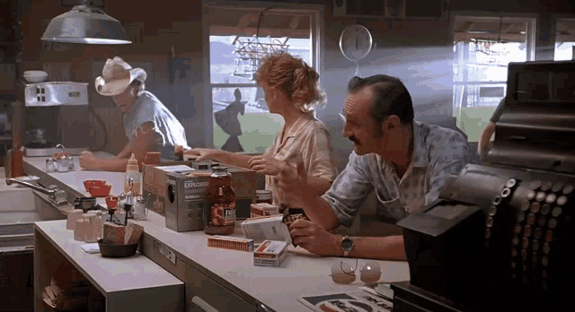 a man in a cowboy hat sits at a counter in a diner talking to a woman and another man