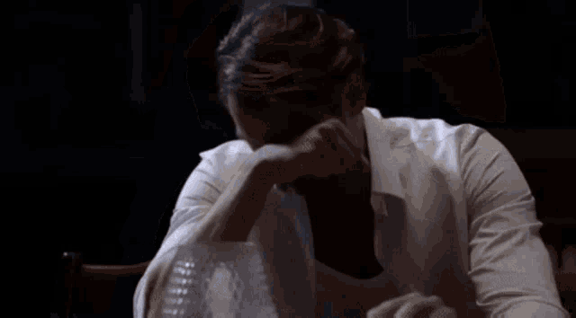 a man in a white shirt is sitting in a chair in a dark room with his shirt open .